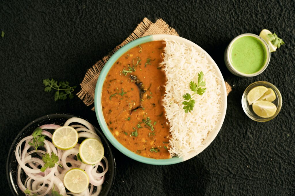Top view of a traditional Indian meal with rice, curry, and fresh garnishes, perfect for lunch or dinner.