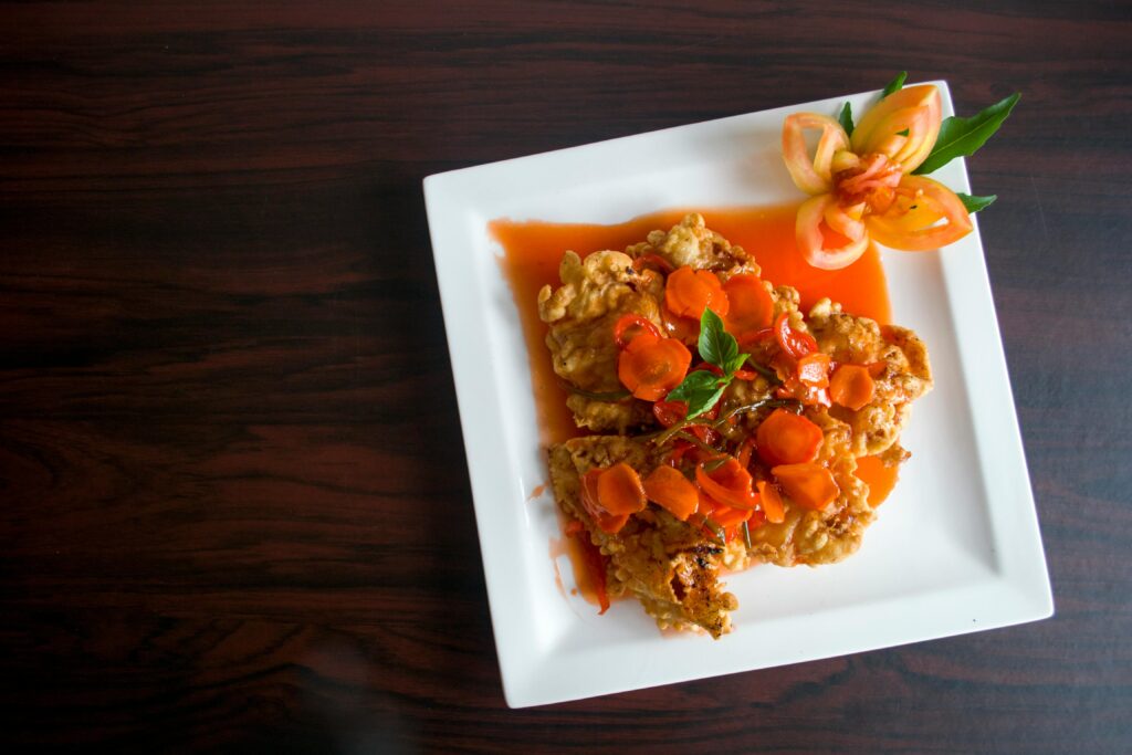 Crispy fried chicken topped with carrots and a floral tomato garnish.